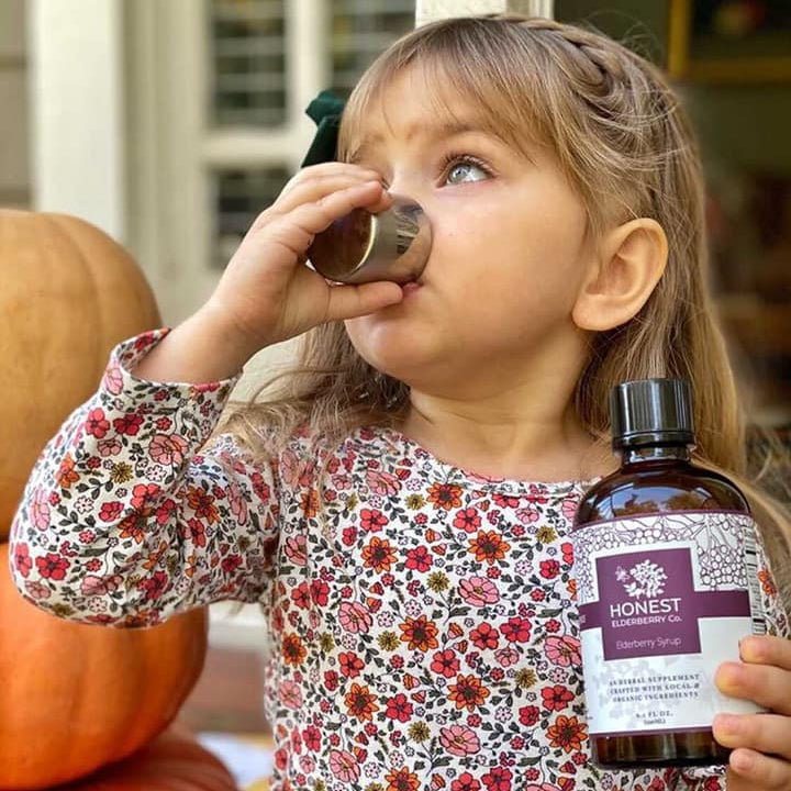 young girl drinking honest elderberry syrup